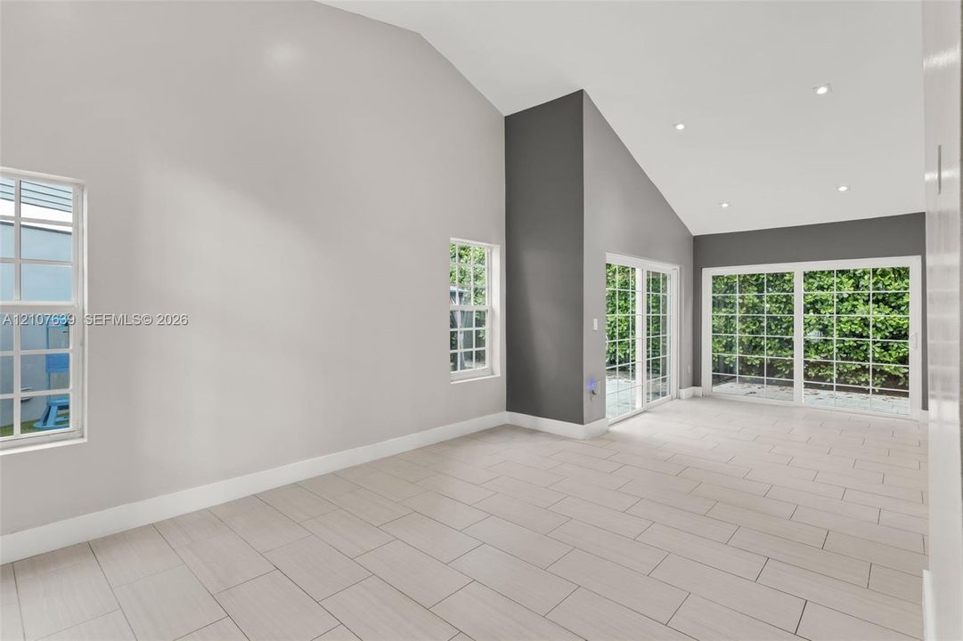 Vaulted ceiling with recessed lighting, tile flooring, and dual sliding glass doors