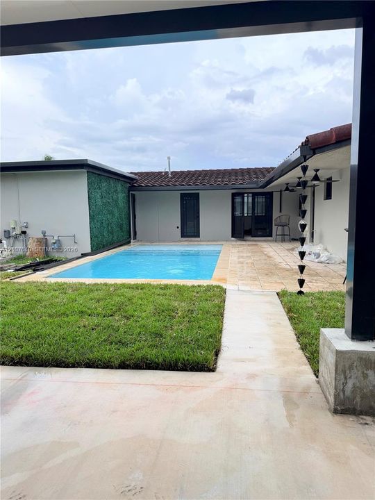 Private courtyard featuring an in-ground swimming pool, stone-paver patio, manicured lawn, and decorative green wall paneling