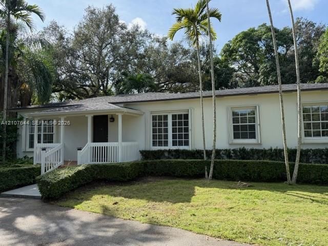 Single-story residence featuring a smooth stucco exterior, covered front porch with white railing, grid-pattern windows, and asphalt shingle roofing