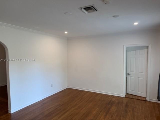 Neutral-toned interior space featuring wood-finish flooring, recessed lighting, crown molding, a decorative arched entryway, and a six-panel door