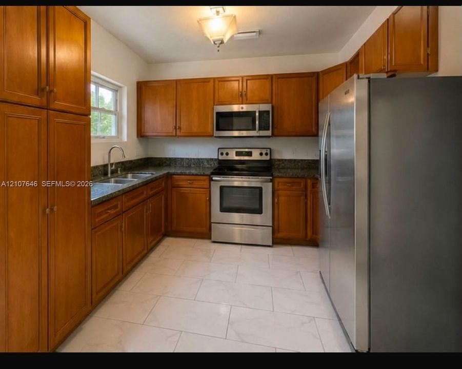 Kitchen featuring wood cabinetry, stone-surface countertops, stainless steel appliances, and large-format tile flooring