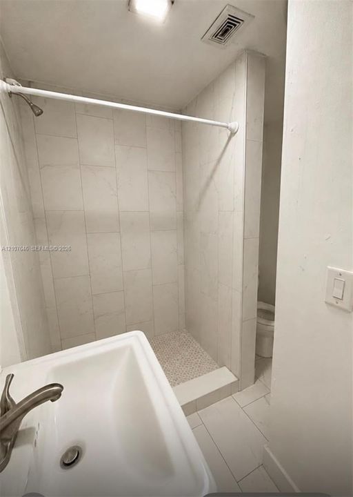 Shower featuring floor-to-ceiling large-format tile surround, mosaic tile flooring, and a wall-mounted sink with a metallic finish faucet