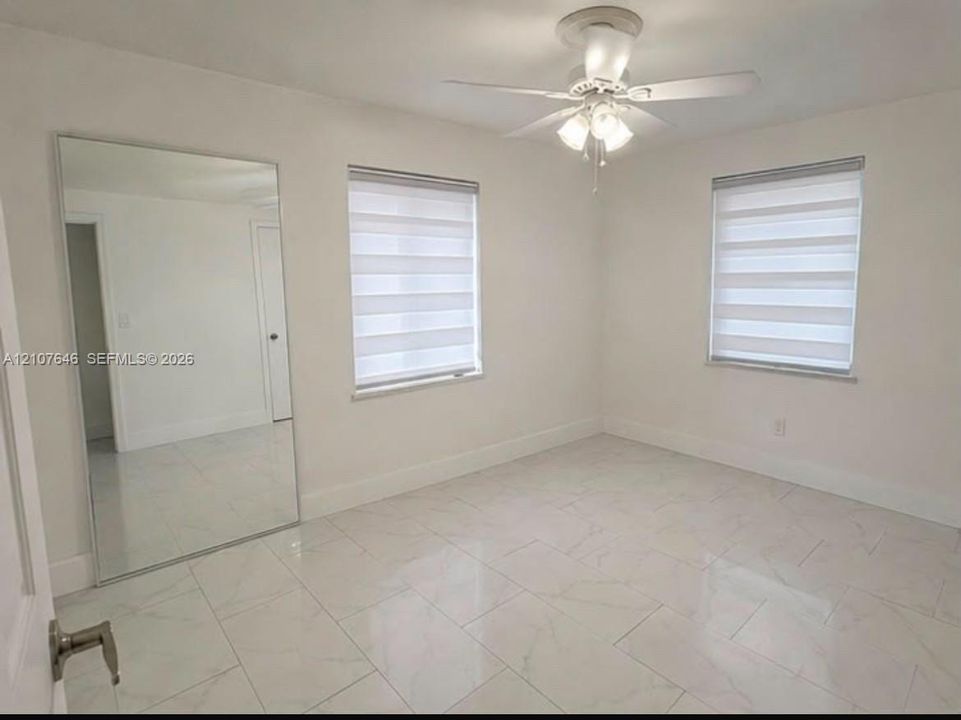 Large-format tile flooring, dual-pane windows with integrated adjustable shades, wall-mounted mirror panel, and ceiling-mounted light fixture with fan