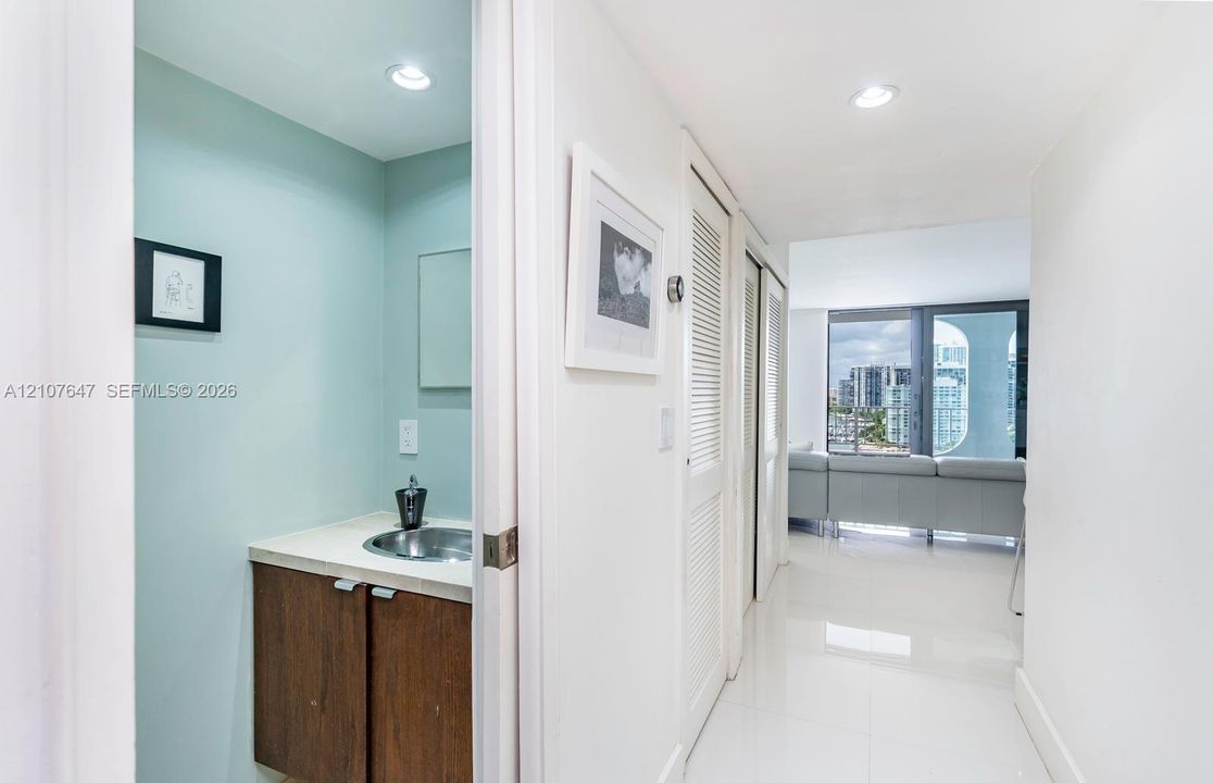 Bathroom vanity featuring a solid-surface countertop and integrated metal sink, paired with wood-finish cabinetry, louvered closet doors, and polished tile flooring
