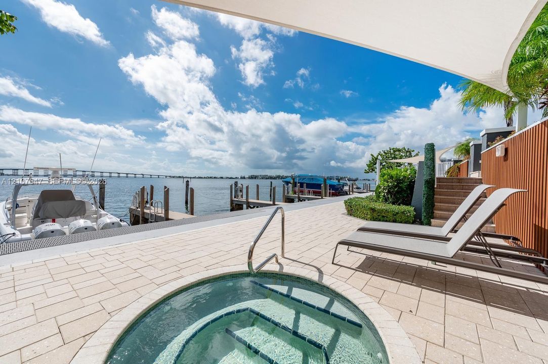 Waterfront terrace featuring a stone-paved deck, in-ground spa, private boat dock, and vertical slat wood-finish wall paneling