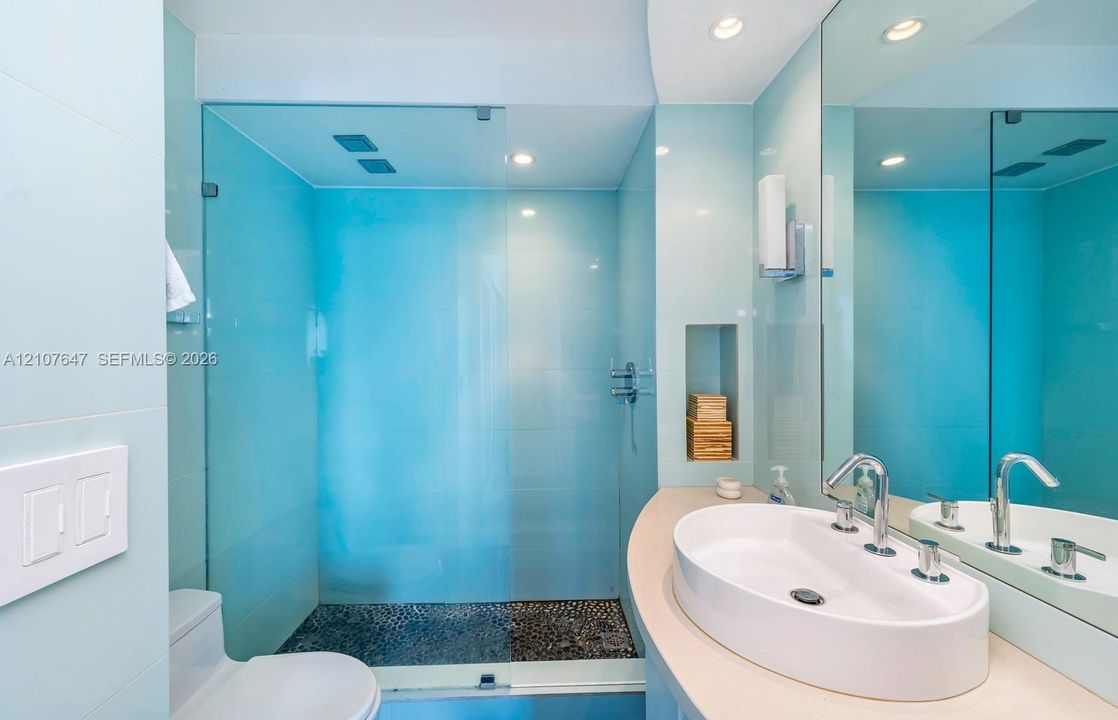 Bathroom featuring a glass-enclosed shower with pebble-stone flooring, a curved vanity countertop, an integrated vessel sink with polished chrome fixtures, and a recessed wall niche