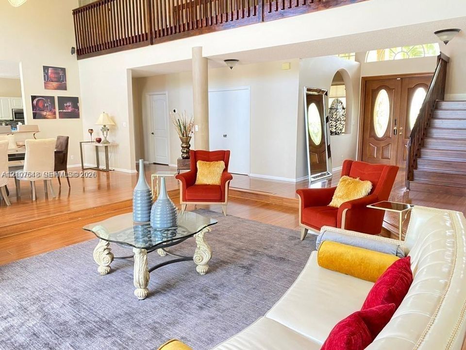 Sunken living area featuring wood-finish flooring, a double-height ceiling, a wooden staircase with a slatted railing, and arched architectural detailing