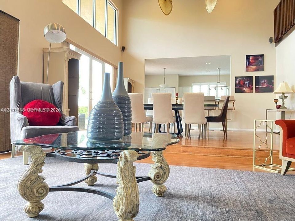 Living area featuring double-height ceilings, floor-to-ceiling windows, wood-finish flooring, and a raised platform