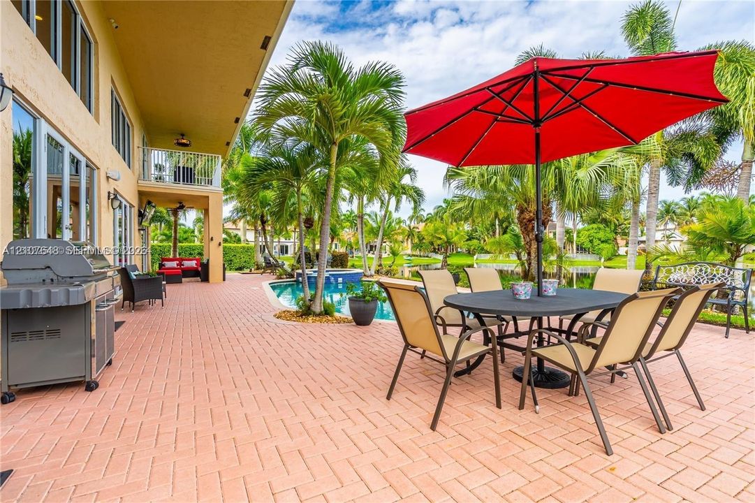 Brick-paved patio featuring an inground swimming pool, integrated spa, built-in outdoor grill station, and mature palm trees