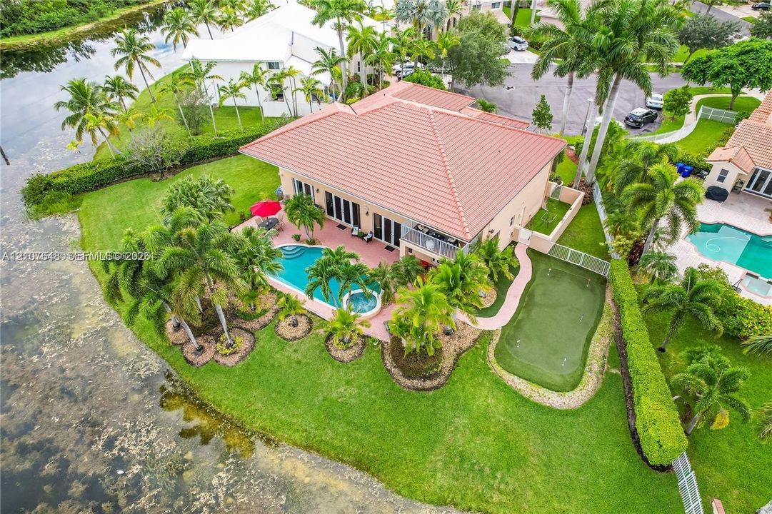 Waterfront property featuring a tile roof, an in-ground pool with integrated spa, a paved patio, and a putting green