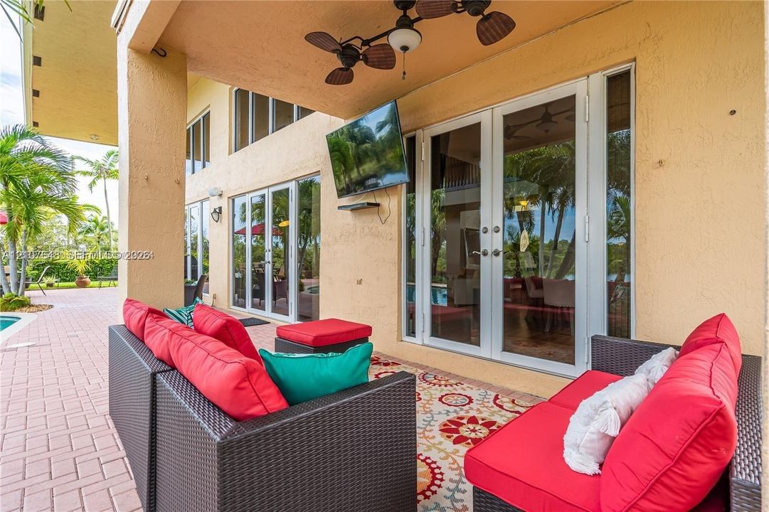 Covered patio featuring paver flooring, stucco wall finish, wall-mounted television, and dual sets of glass French doors