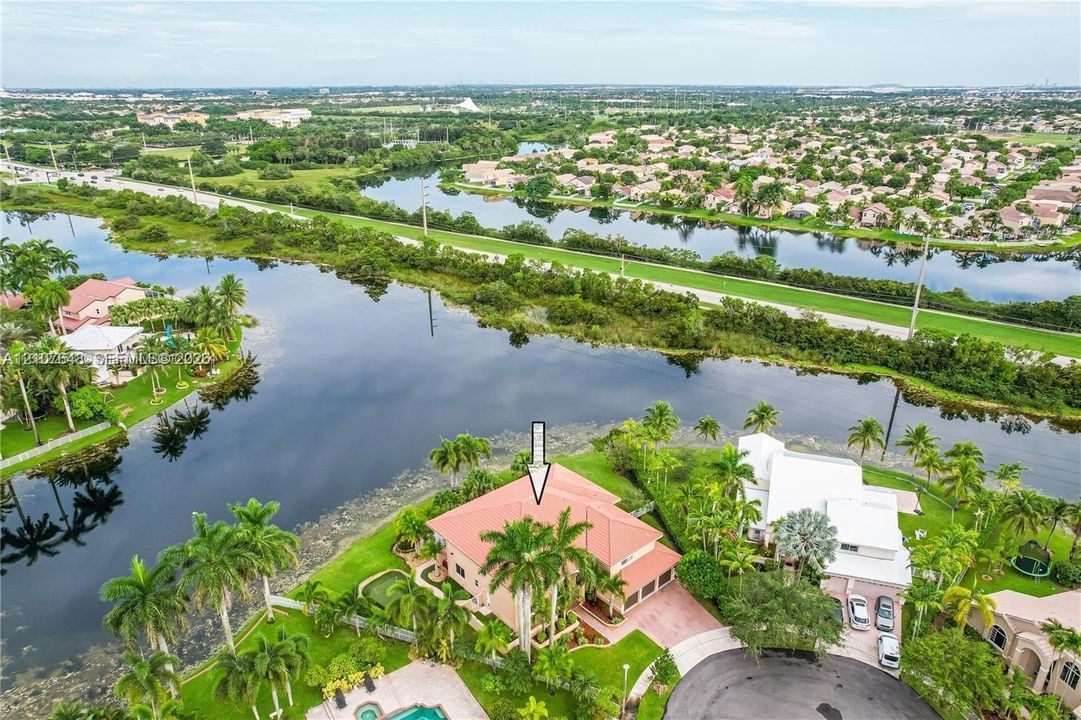 Waterfront residence featuring a tiled roof, multi-car garage, paved driveway, and mature landscaping situated along a canal