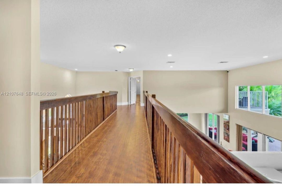 Open walkway featuring wood-finish flooring, a decorative wood-slat railing, recessed lighting, and flush-mount fixtures