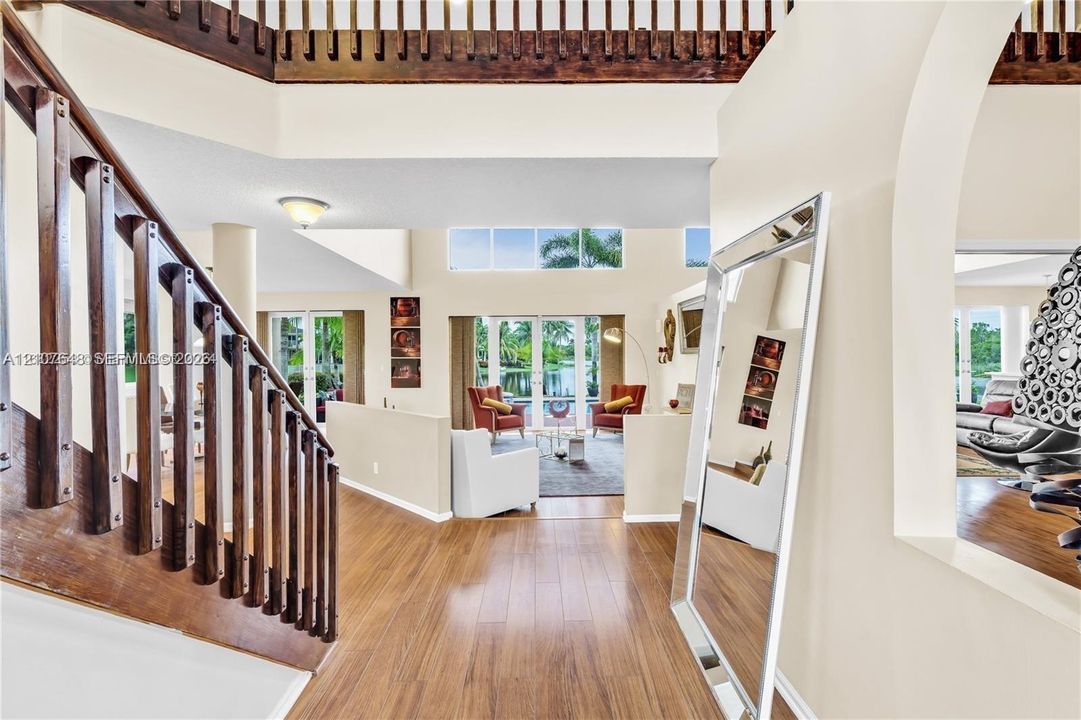 Two-story entryway featuring high ceilings, wood-finish flooring, a wooden staircase with vertical balusters, and arched structural openings