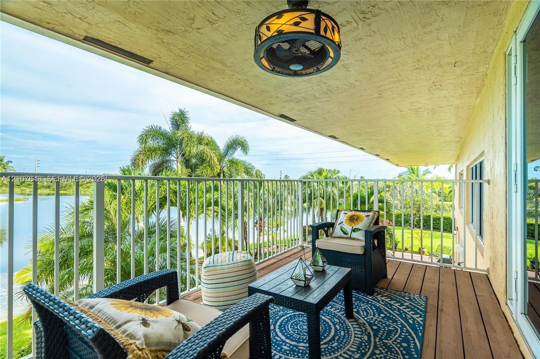 Covered balcony featuring white vertical railings, wood-finish decking, and decorative flush-mount ceiling lighting