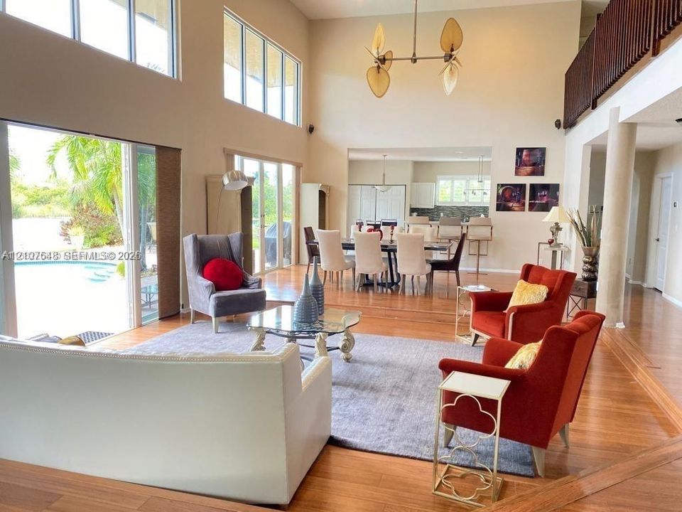 Double-height ceiling with floor-to-ceiling windows, wood-finish flooring, metal multi-arm chandelier, and sliding glass doors