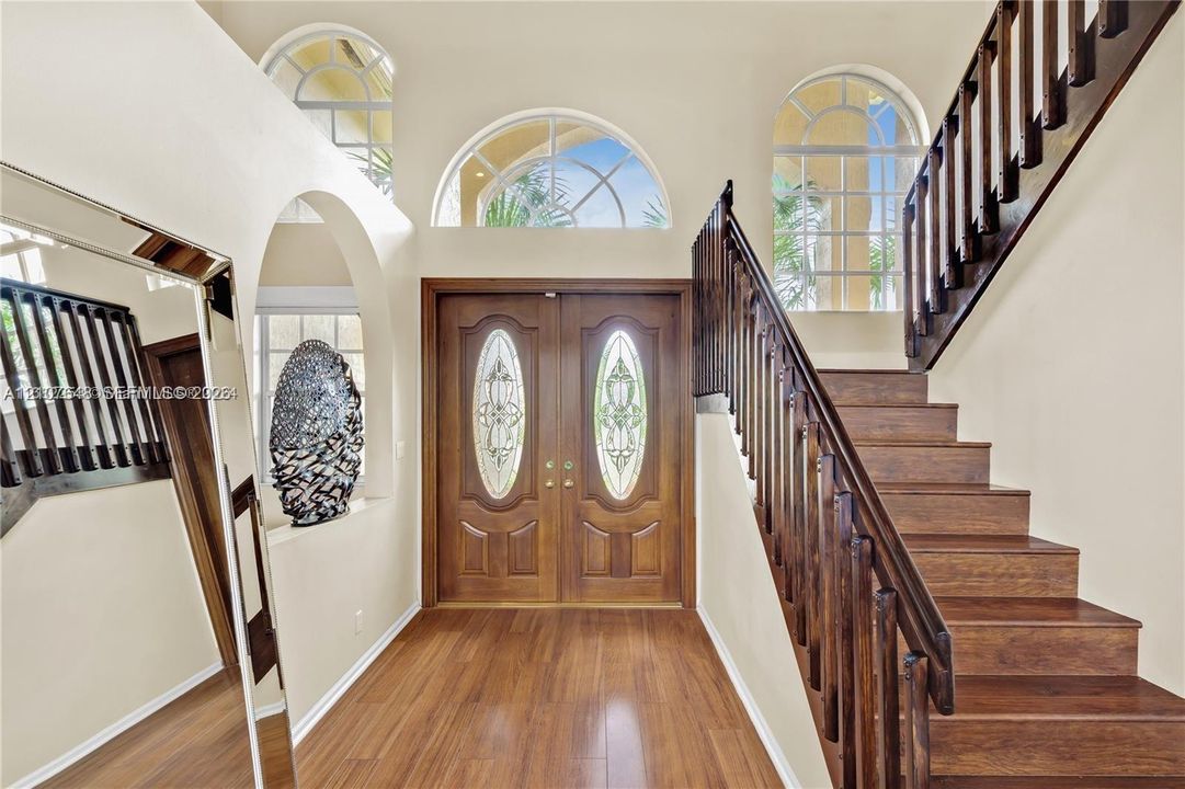 Entryway featuring double wood-paneled doors with glass inserts, arched windows, wood-finish flooring, and a staircase with a dark wood railing