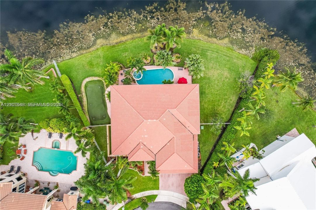 Aerial perspective of a waterfront property featuring a tile roof, an in-ground swimming pool with an attached spa, and a dedicated putting green
