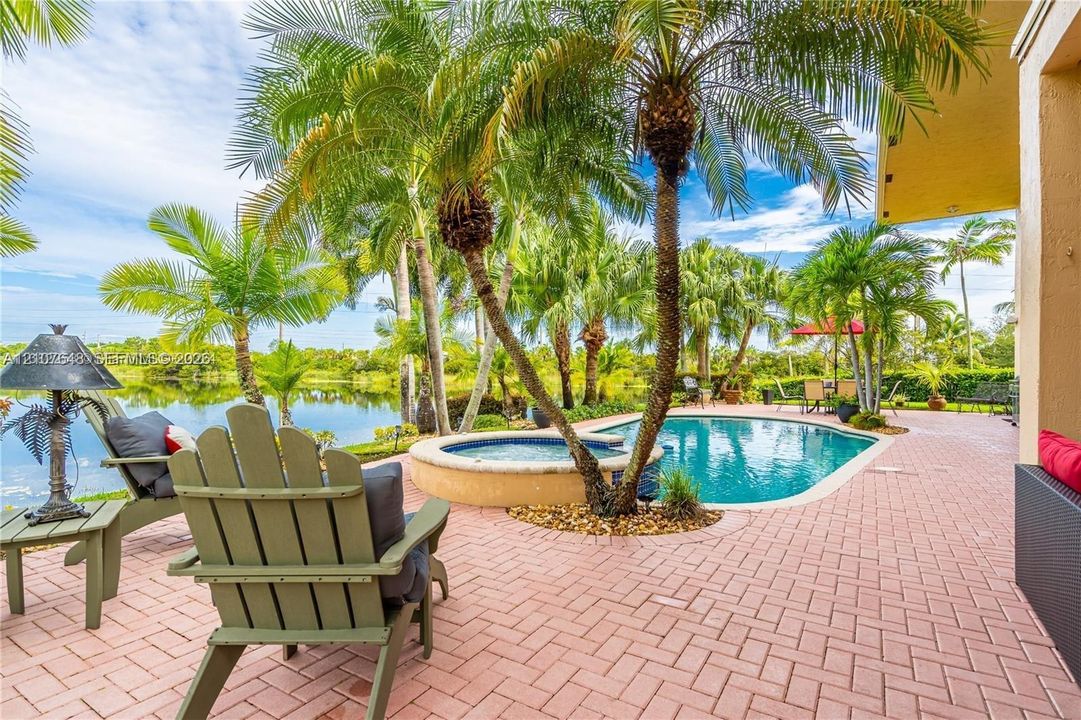 Brick-paver patio featuring a swimming pool, integrated spa, mature palm trees, and waterfront perimeter