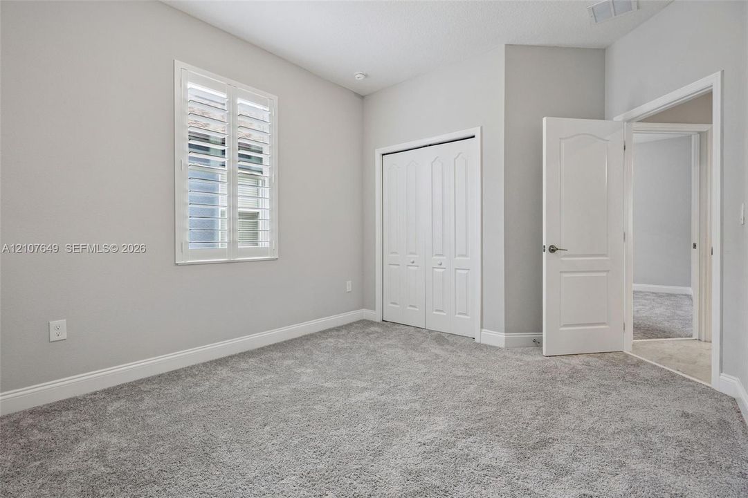 Room featuring neutral wall tones, vaulted ceilings, carpeting, louvered window shutters, and a double-panel interior door
