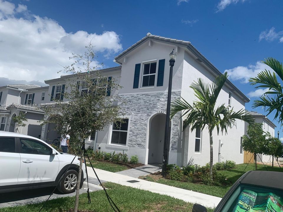 Two-story exterior featuring a light-toned stucco finish, stacked stone facade detailing, arched entryway, and dark blue shutters
