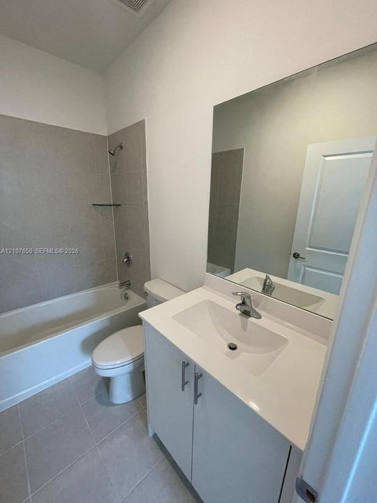 Bathroom featuring a vanity with a white countertop and integrated sink, full-width wall mirror, tile-surround bathtub, and neutral ceramic floor tiling