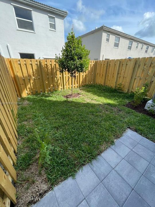 Enclosed outdoor area featuring a wood privacy fence, paved patio, and grass lawn
