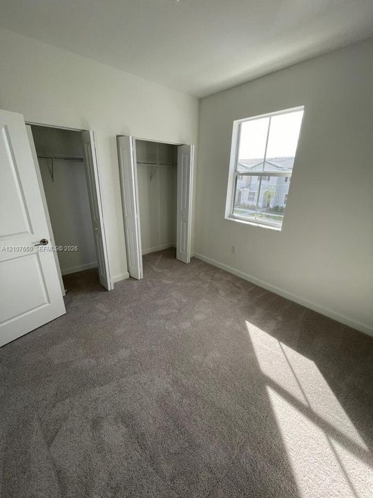 Neutral wall palette, carpeting, dual-door closets with shelving, and window providing natural light