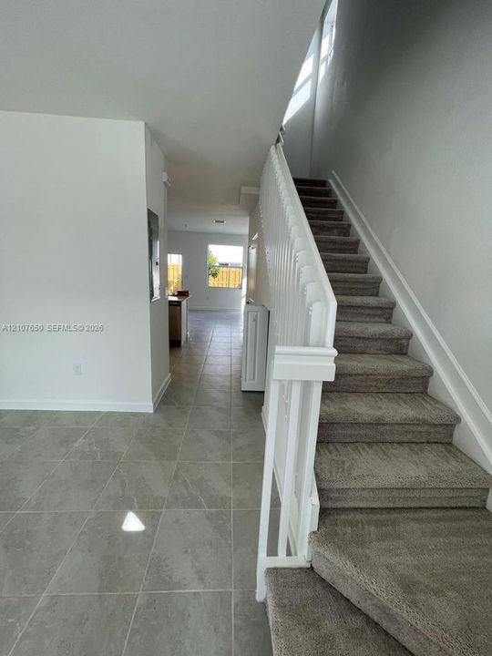 Neutral-toned tile flooring, carpeted staircase with white painted wood balusters, and minimalist wall finishes