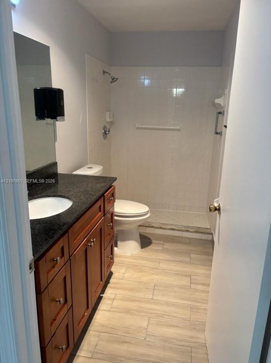 Bathroom featuring wood-finish cabinetry, dark countertop with an integrated basin, tile flooring, and a tiled shower stall