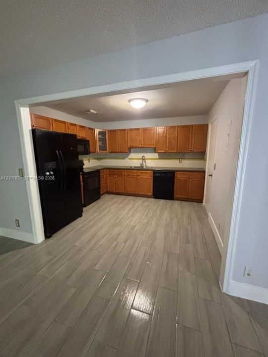 Kitchen featuring wood-finish cabinetry, black appliances, solid-surface countertops, and wood-finish tile flooring
