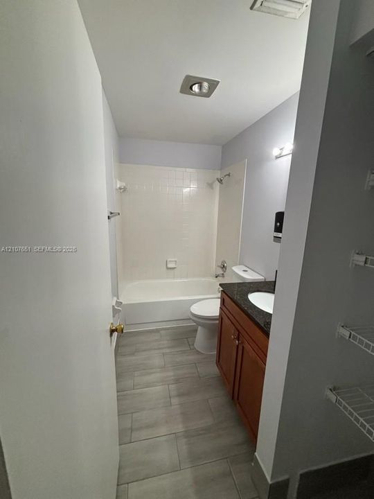 Bathroom featuring a vanity with a stone-finish countertop, under-mount sink, wood-finish cabinetry, tile flooring, and a tub-shower combination with tile surround