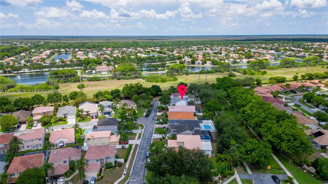 Aerial view of the residential property featuring a backyard swimming pool, paved driveway, multi-level roof structure, and surrounding landscape
