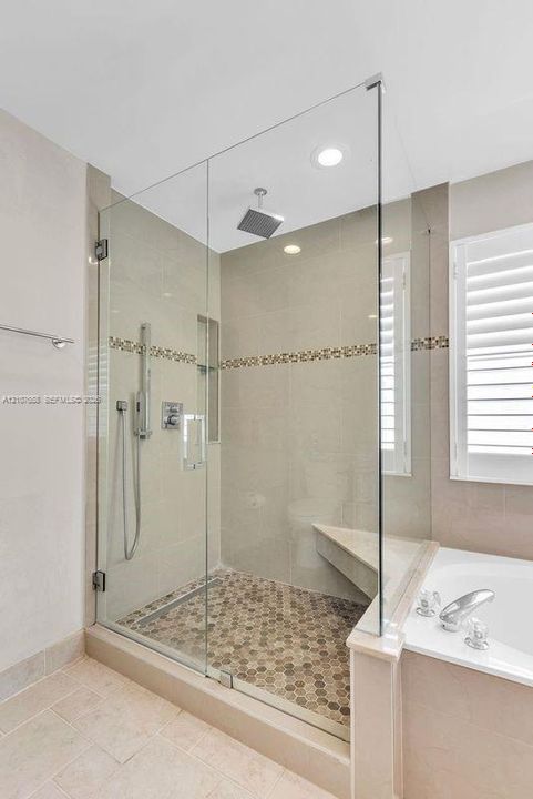 Walk-in shower featuring a frameless glass enclosure, rainfall showerhead, handheld sprayer, built-in corner bench, and mosaic tile flooring with decorative accent banding