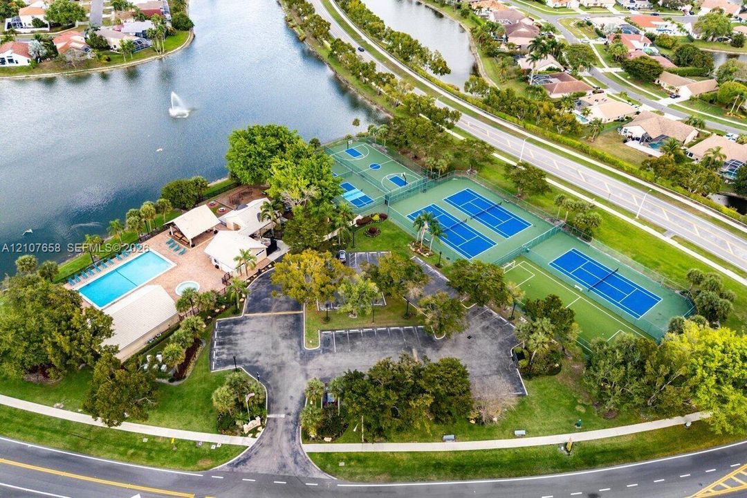 Recreational facility featuring a swimming pool, multiple tennis courts, a basketball court, and paved parking area situated on a waterfront lot