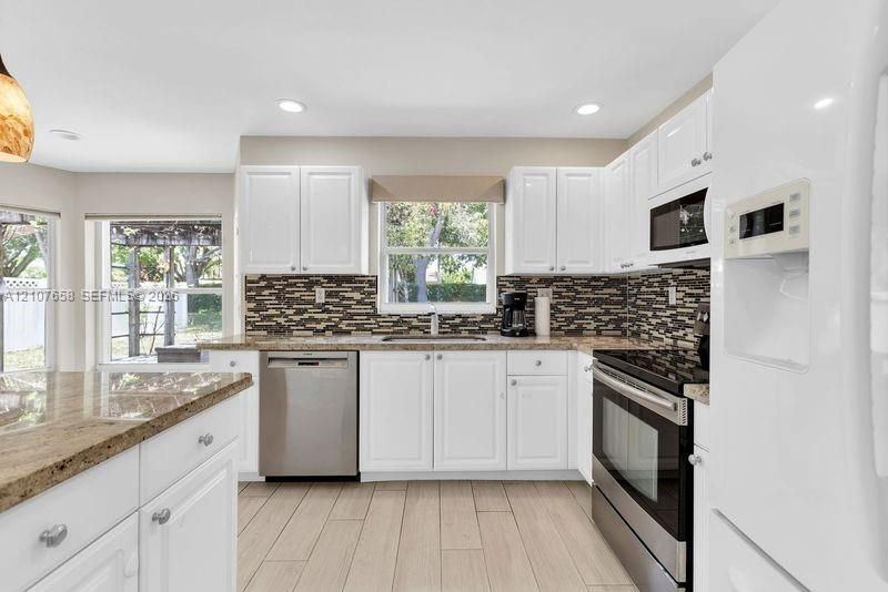 Kitchen featuring white cabinetry, stone countertops, stainless steel appliances, multi-tonal mosaic tile backsplash, and wood-finish flooring