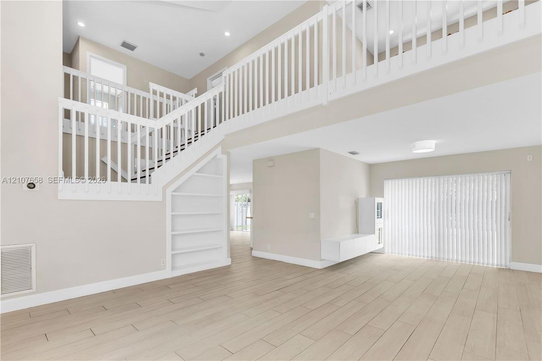 Two-story foyer with a mezzanine balcony, wood-finish flooring, white staircase featuring open shelving, and a wall-mounted floating storage unit