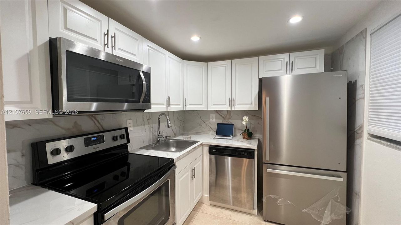 Kitchen featuring white shaker-style cabinetry, stainless steel appliances, stone-finish countertops, full-height decorative backsplash, and recessed lighting