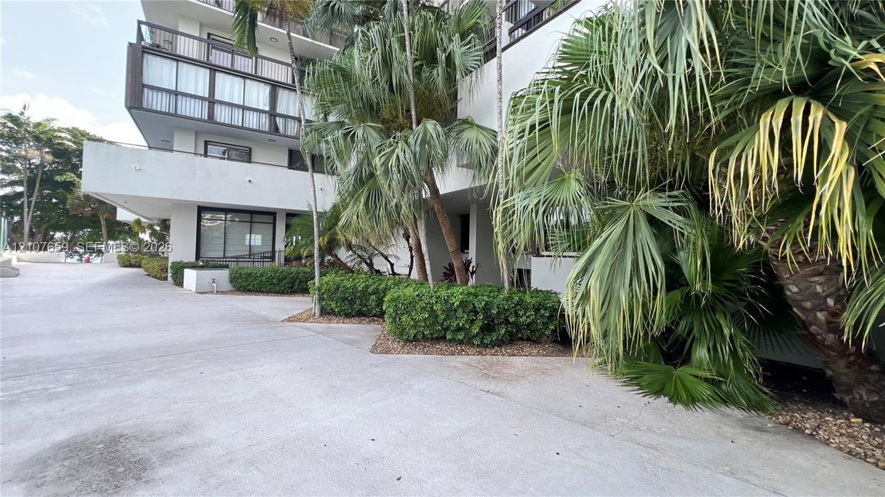 Multi-story building exterior featuring balconies with railings, concrete surfacing, and established palm tree landscaping
