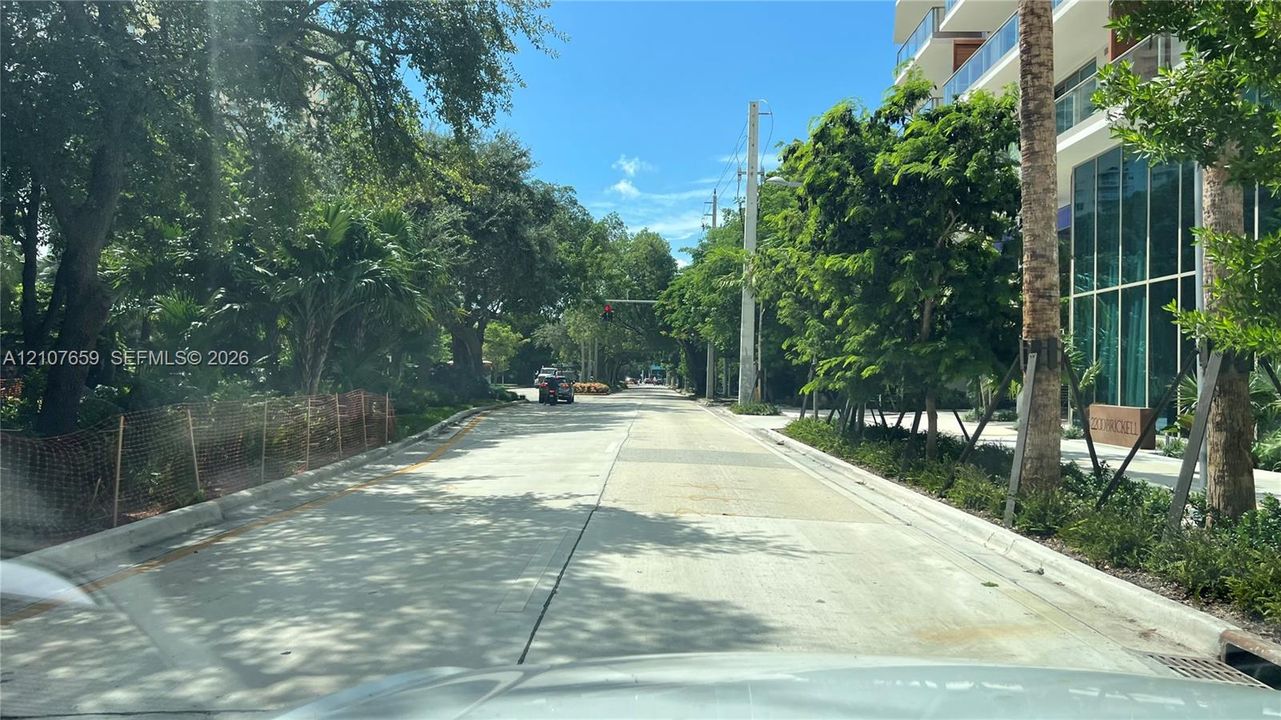 Tree-lined thoroughfare featuring concrete paving, mature landscaping, and modern glass-facade structures