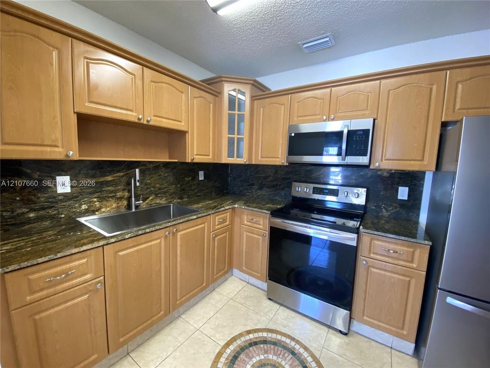 Kitchen featuring light wood-finish cabinetry,  stone countertops, stainless steel appliances, a single-basin undermount sink, and tiled flooring