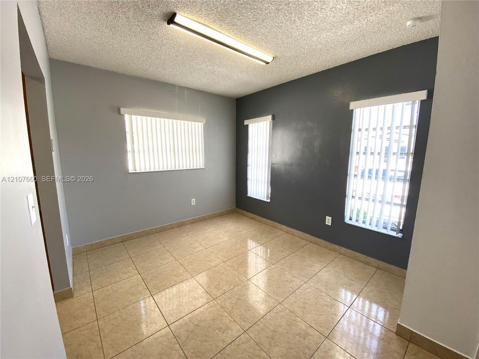 Neutral-toned interior featuring square tile flooring,  three windows with vertical blinds, and a linear overhead light fixture