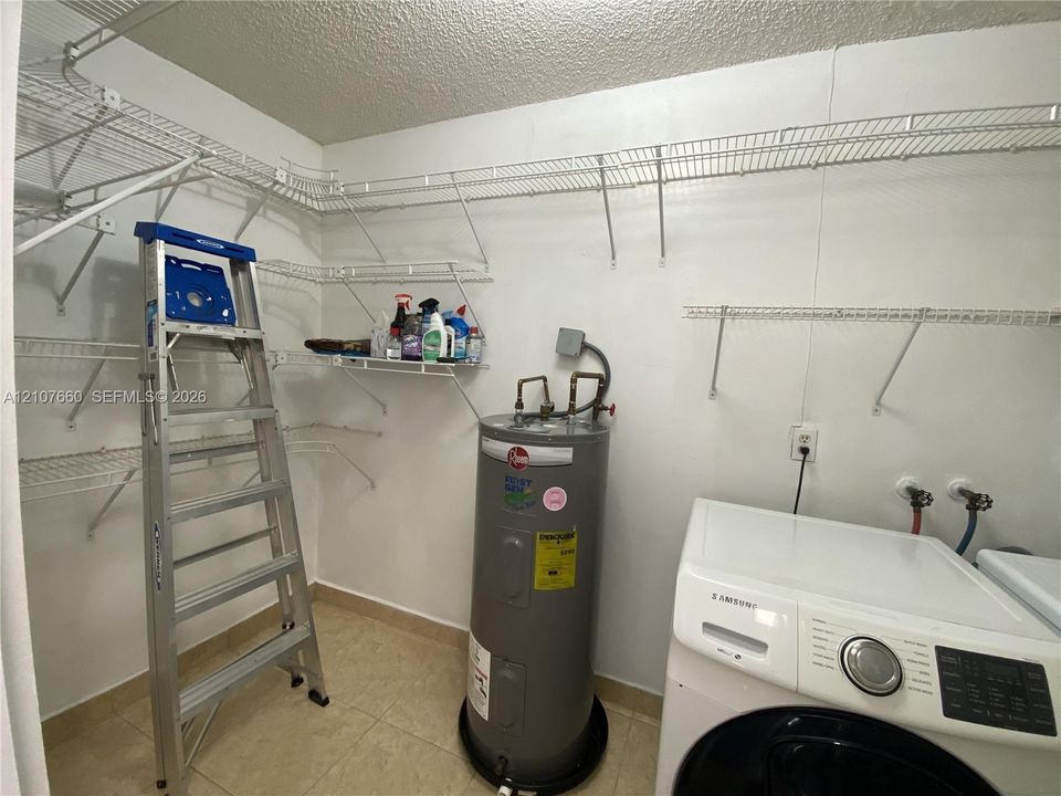 Utility area featuring tile flooring, white-coated wire shelving, a water heater, and integrated laundry hookups