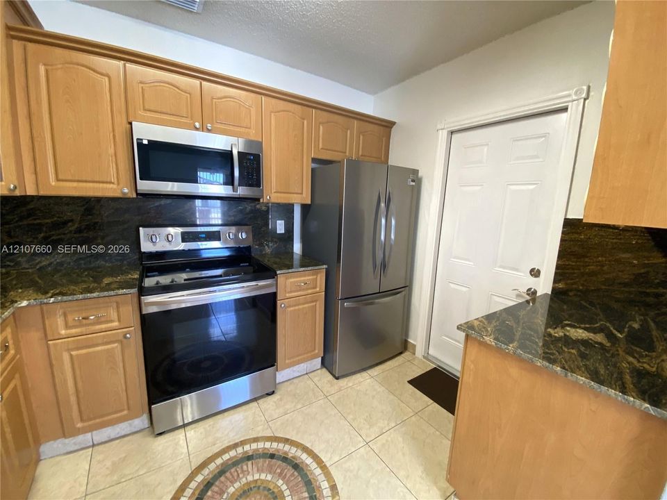 Kitchen featuring natural wood cabinetry, stone-finish countertops, stainless steel appliances, and tiled flooring