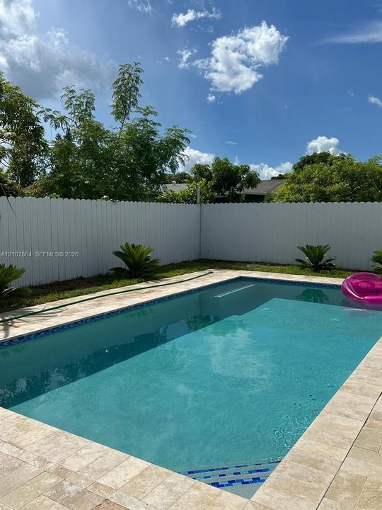 In-ground swimming pool featuring tile coping, a stone-finish paver deck, and a white privacy fence