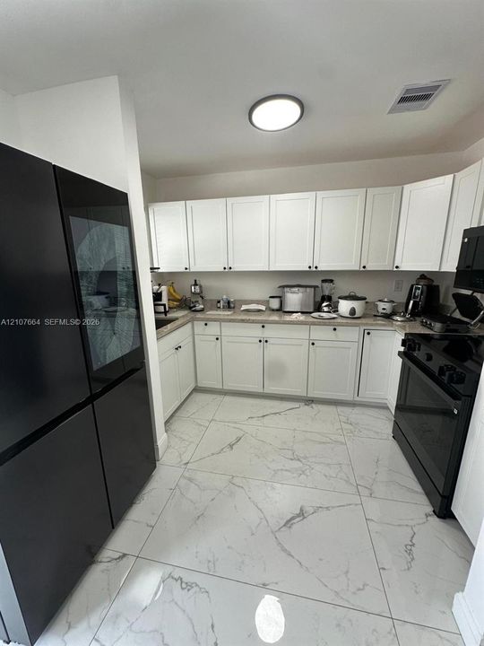 Kitchen featuring white shaker-style cabinetry, solid-surface countertops, large-format tile flooring with veined detailing, and black appliances