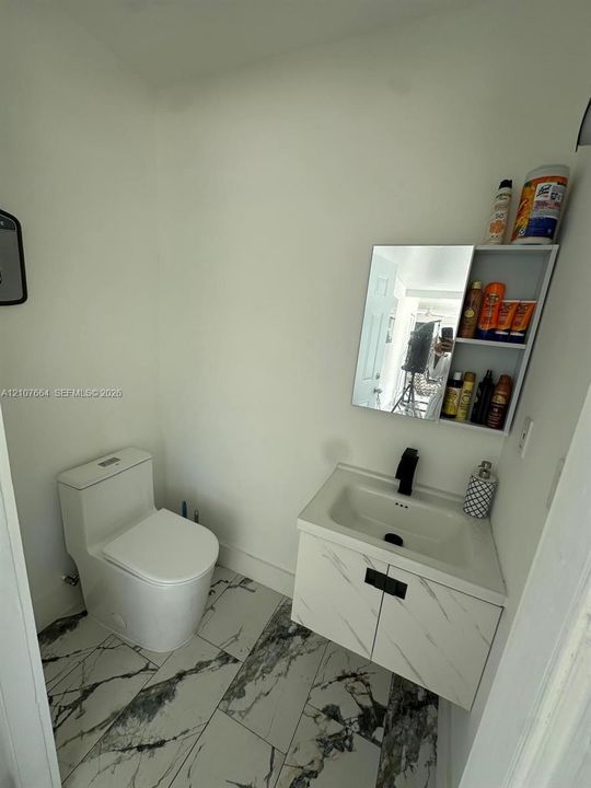 Floating vanity with stone-patterned cabinetry, rectangular sink, matte black faucet, and large-format porcelain tile flooring