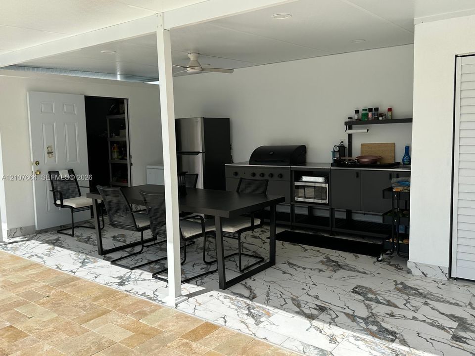 Covered outdoor kitchen area featuring high-contrast tile flooring, matte black cabinetry, a built-in grill, and an integrated ceiling fan