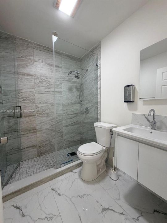 Bathroom featuring a walk-in shower with floor-to-ceiling stone-look tile, a frameless glass enclosure, a white vanity with an integrated sink, and large-format porcelain tile flooring