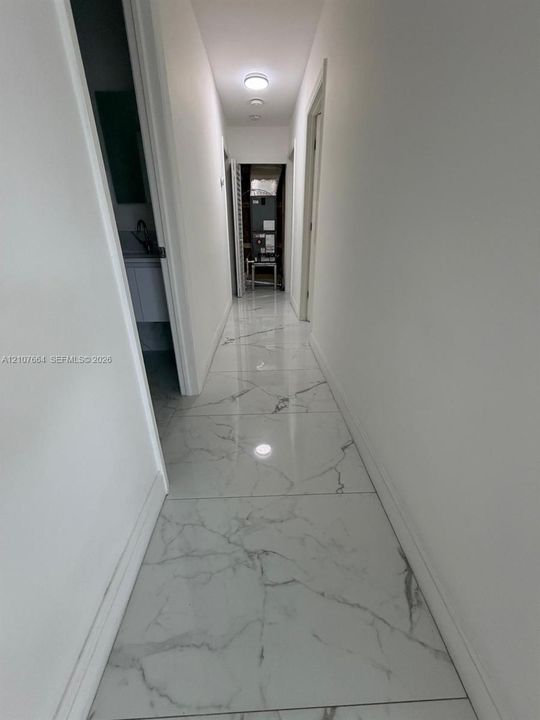 Hallway featuring large-format, white, veined tile flooring and flush-mount ceiling lighting